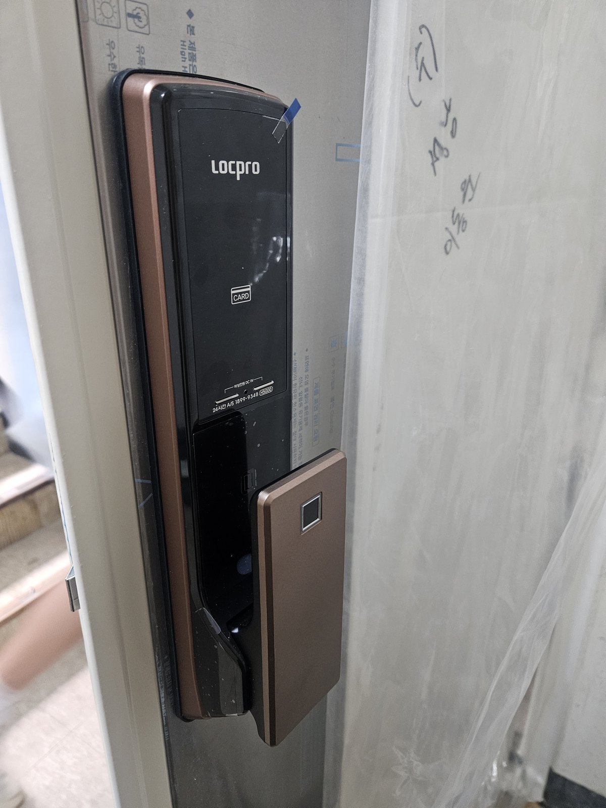 부천시 도당동 출장 — 투명 비닐을 씌운 문에 단 구리빛 테두리의 푸시풀 도어락과 지문 표시가 있는 손잡이판